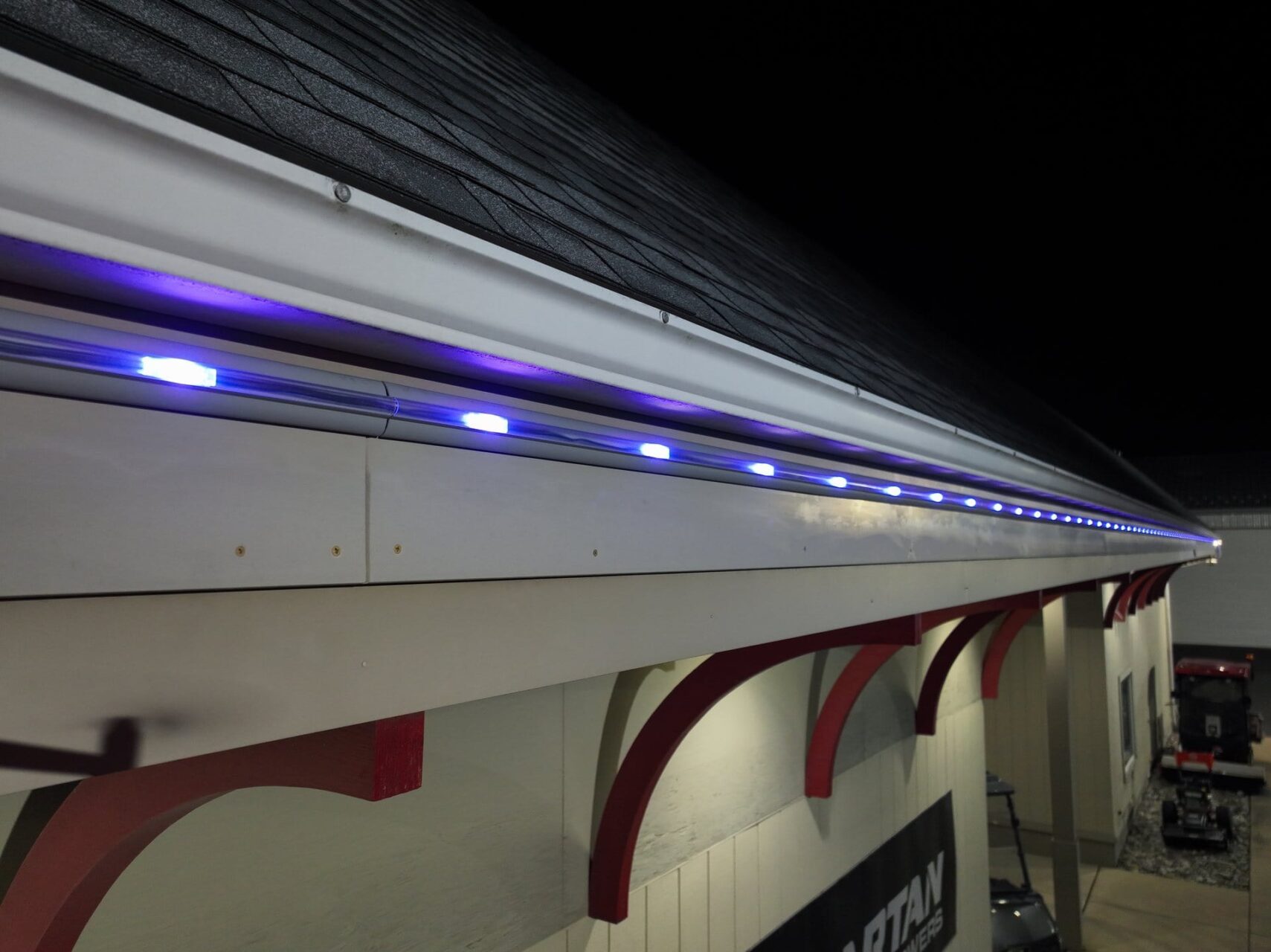 Blue LED lights are installed along the edge of a roof at night, illuminating the trim.