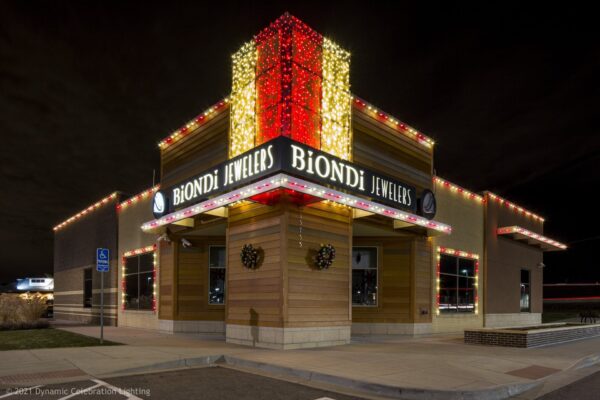 Jewelry store at night with festive lights, a red and gold vertical display, and two holiday wreaths.