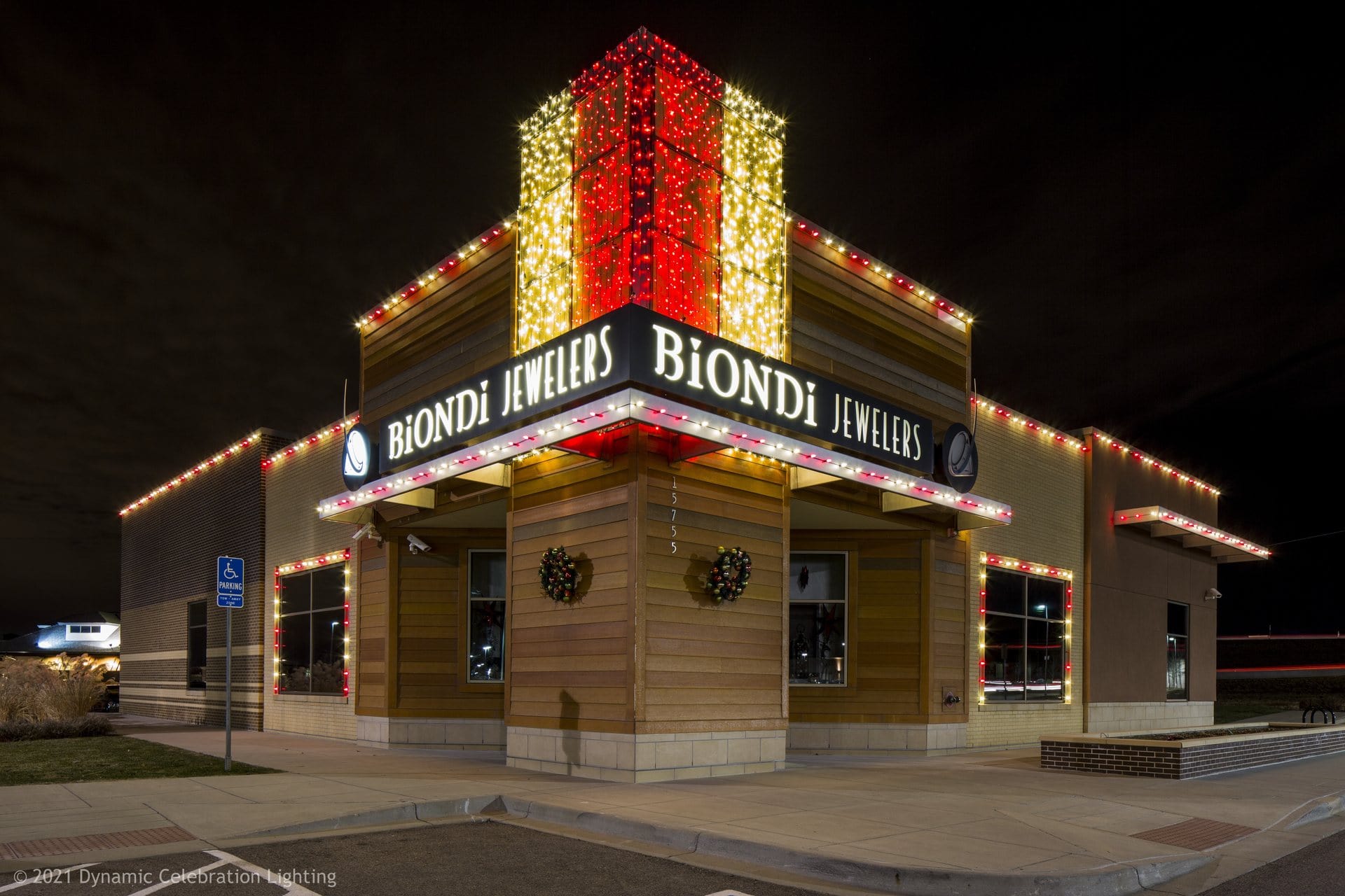 Jewelry store at night with festive lights, a red and gold vertical display, and two holiday wreaths.