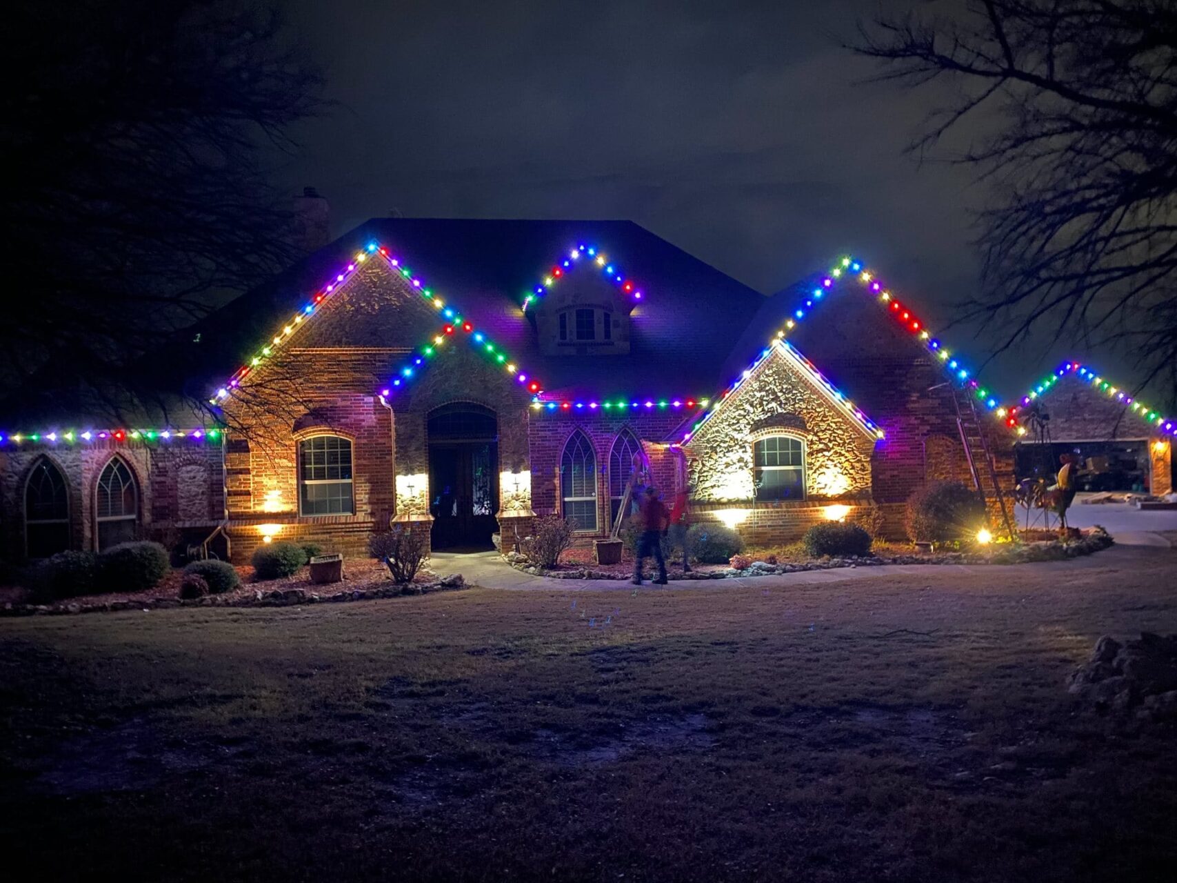 A house at night decorated with colorful holiday lights along the roof and porch.