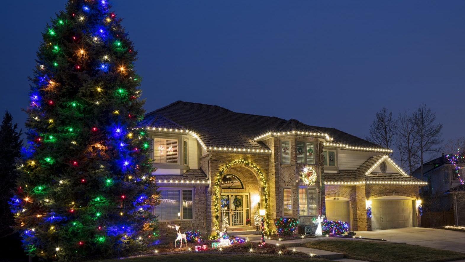 A brick house decorated with glowing string lights and a large, multi-colored lighted Christmas tree.