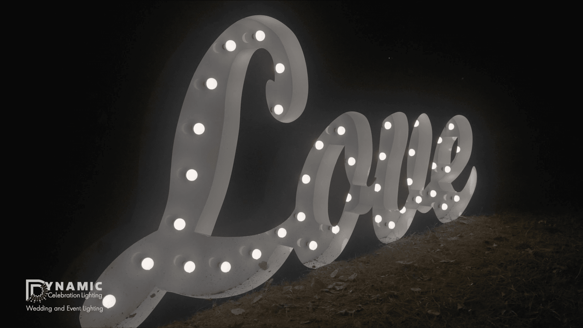 Large marquee Love sign with round white lights, glowing at night on a grassy surface.